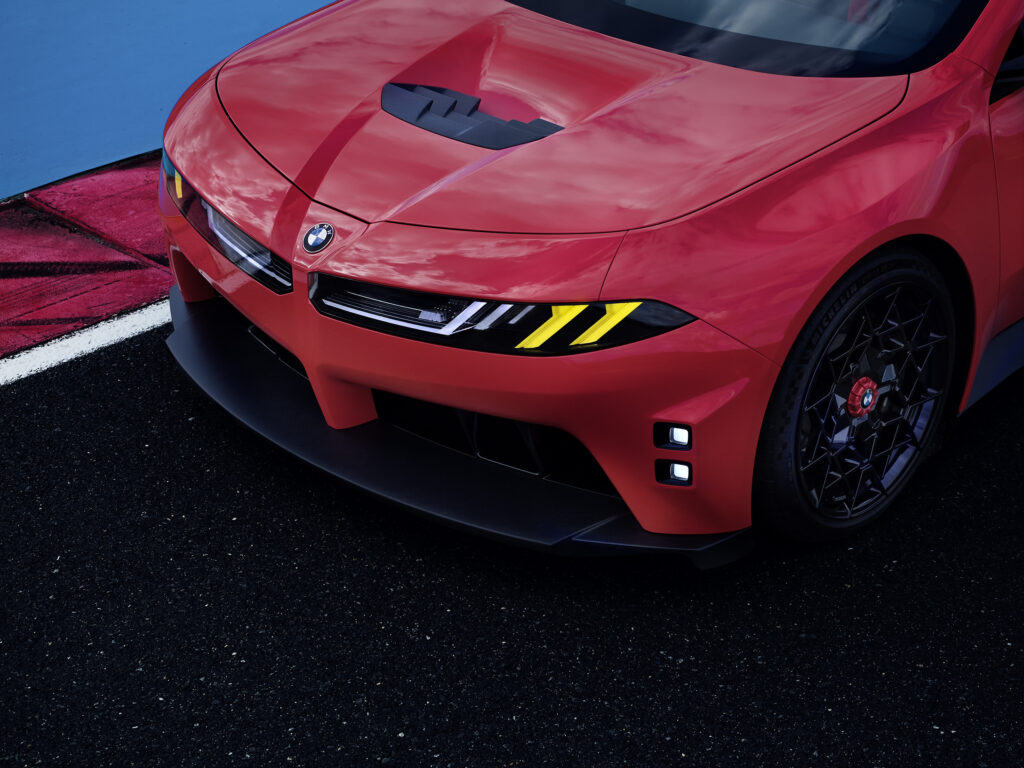Detalle frontal del BMW M Concept Neue Klasse en color Monza Red, con luces M Yellow Lights, salida de aire en el cofre y diseño aerodinámico inspirado en competición.