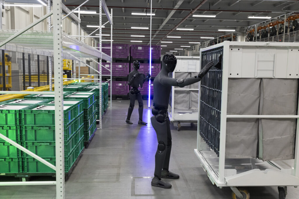Robots humanoides Figure 03 trabajando en un área logística de BMW Group Planta Spartanburg, donde apoyan tareas de secuenciación y manipulación de componentes.