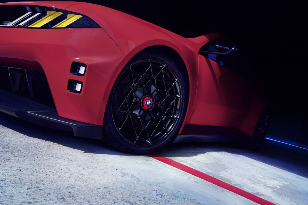 Detalle lateral del BMW M Concept Neue Klasse en color Monza Red, con rueda de tuerca central, luces M Yellow Lights y diseño inspirado en el automovilismo deportivo.